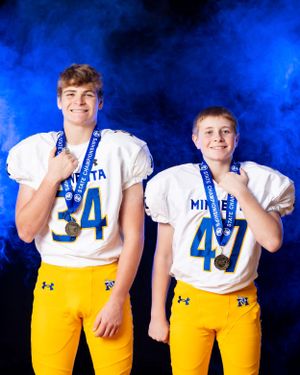 Two youth football players in Minneota white jerseys numbers 34 and 47 proudly display gold medals.