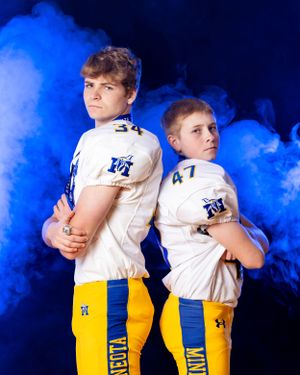 Two Minneota Vikings football players numbers 34 and 47 pose back-to-back in blue smoke.
