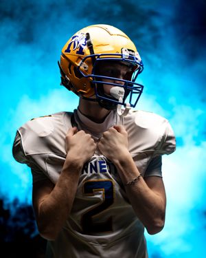 Minneota Vikings football player number 2 adjusts gold helmet chin strap in dramatic blue smoke.