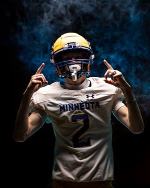 Minneota Vikings football player #2 in white Under Armour jersey points up in blue smoke.