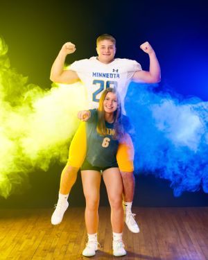 Football player in Minneota number 28 jersey flexes while being carried by a volleyball player number 6.