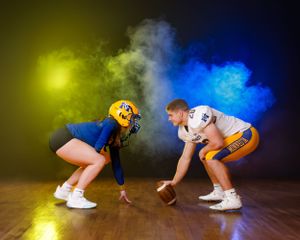 Two Minneota Vikings football players face off in a dramatic yellow and blue smoke-filled indoor setting.