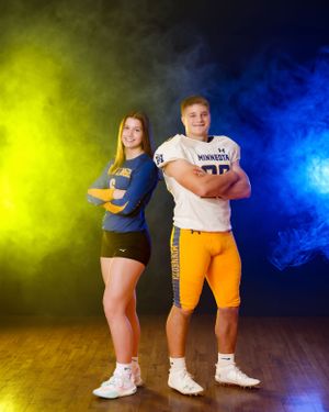 Minneota Vikings football player and female volleyball athlete pose together against colorful yellow and blue smoke.