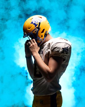 Minneota Vikings football player in gold helmet and white jersey poses dramatically in blue smoke.