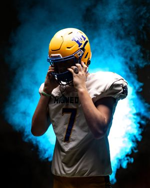 Minneota Vikings football player #7 in gold helmet and white jersey poses in blue smoke.