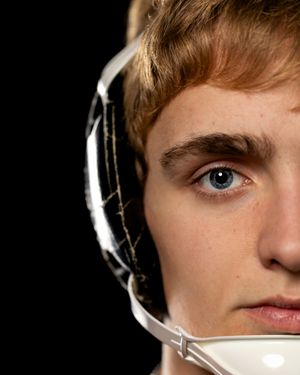 Close-up portrait of a young wrestler wearing a white headgear against a dark background.
