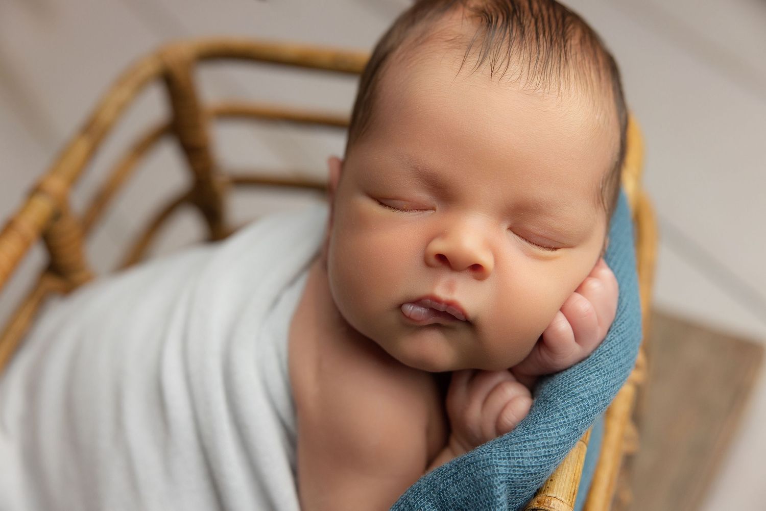 Peaceful newborn baby swaddled in cream wrap sleeping on soft beige blanket during professional newborn photography session.