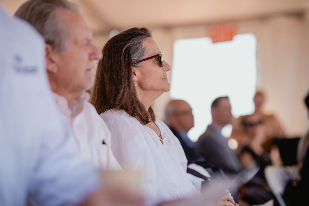 Several people in business attire seated at a conference or meeting under indoor lighting.