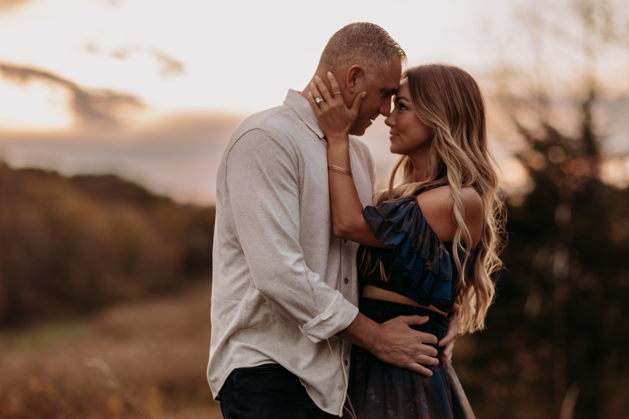 Couple sharing a romantic sunset moment outdoors, touching foreheads with golden light in the background.