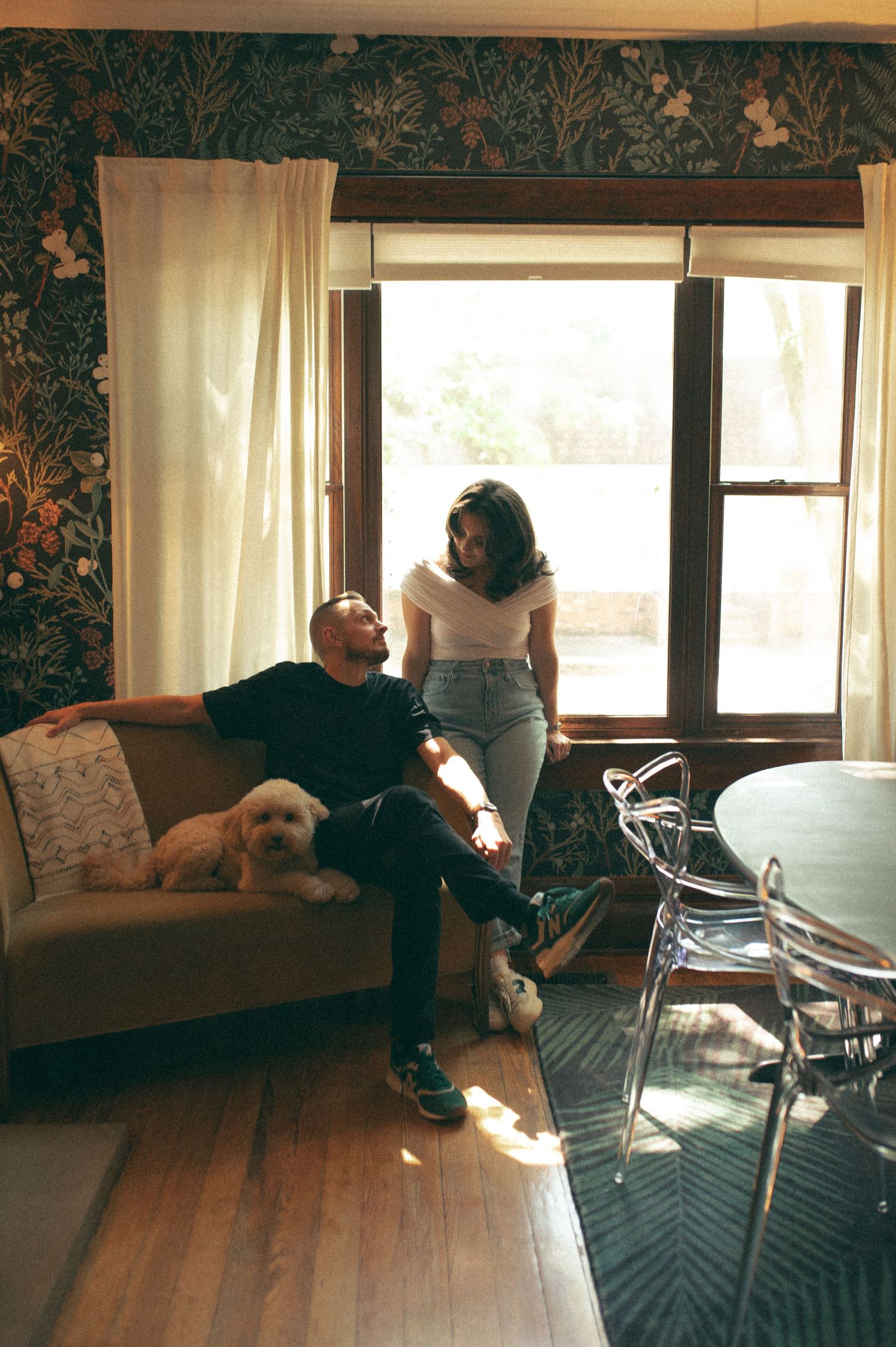 Candid moment in a vintage-styled living room with a small dog, showcasing floral wallpaper and natural window light.