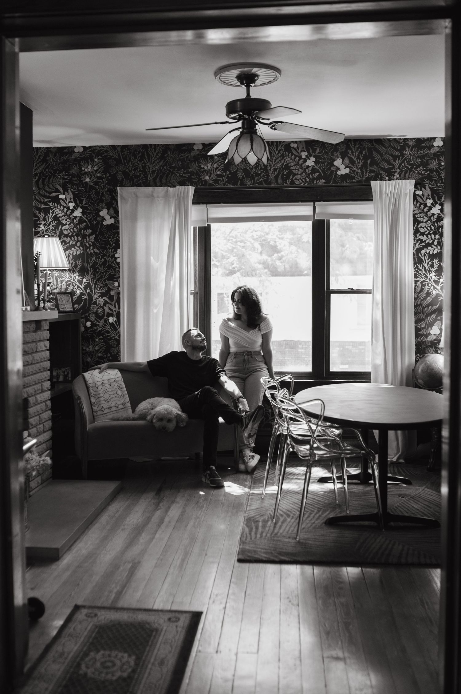 Black and white photo of a living room interior with retro decor and large windows.