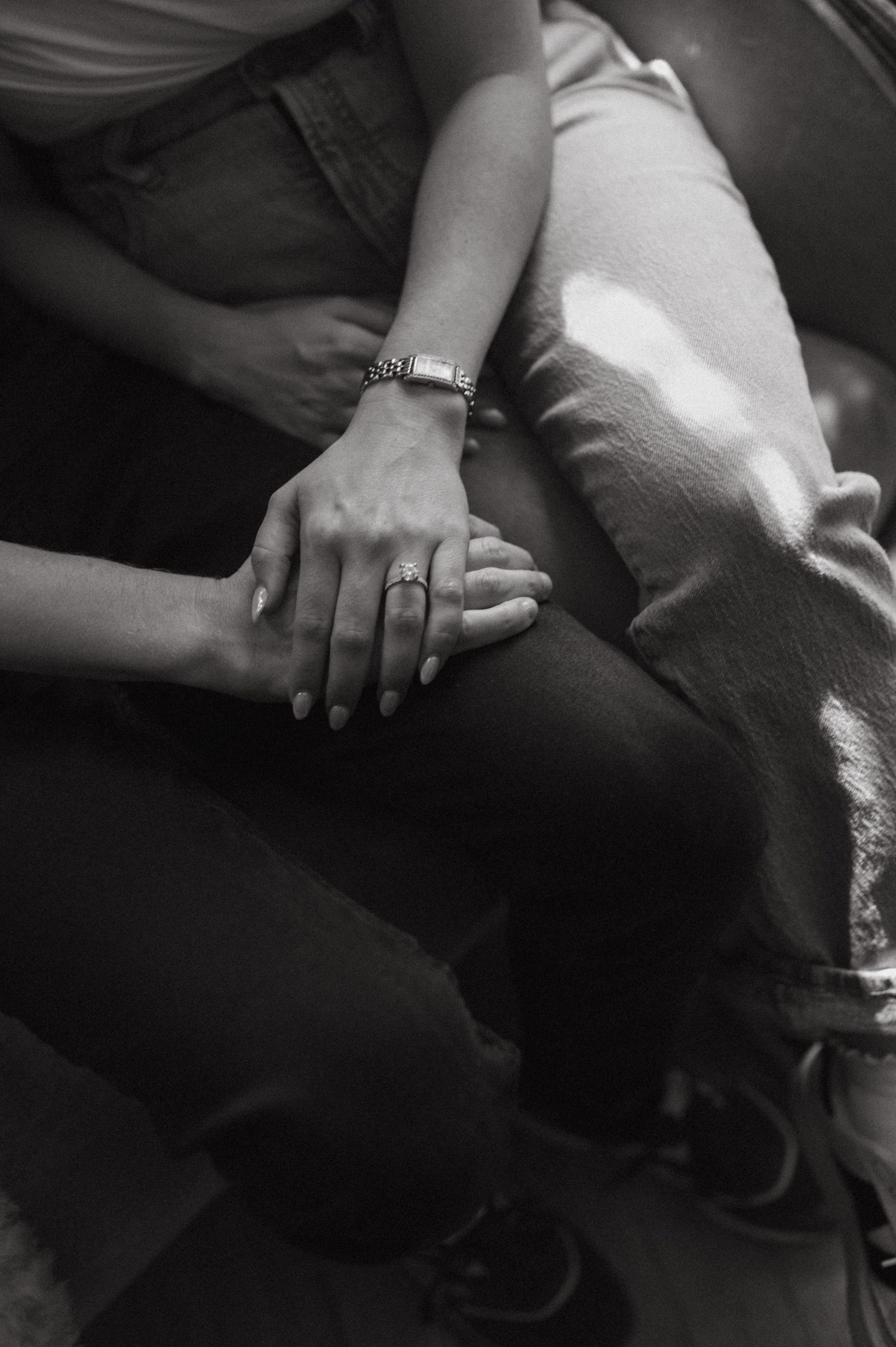 Close-up black and white photo of hands clasped together showing rings and bracelets.