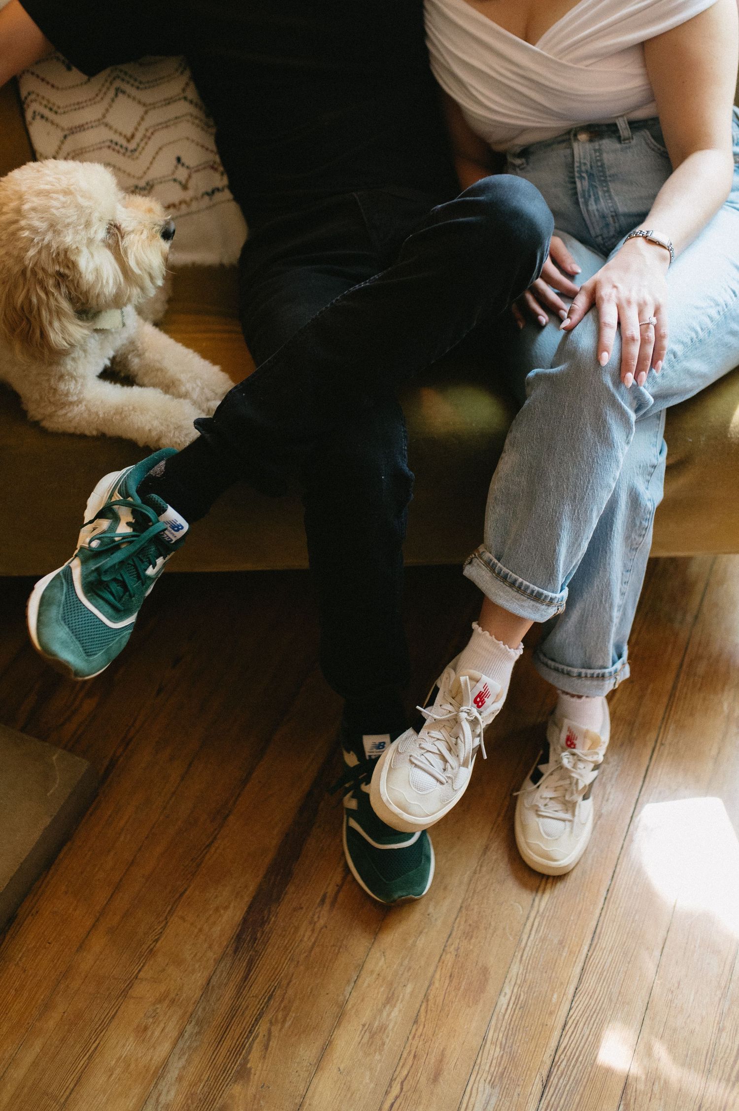 Close-up of casual sneakers and denim with a fluffy white dog nearby on hardwood floor.