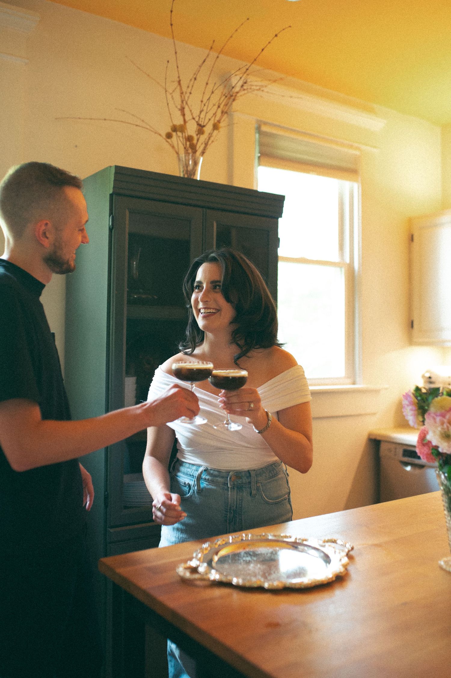 A couple enjoying cocktails together in a bright kitchen with vintage decor.