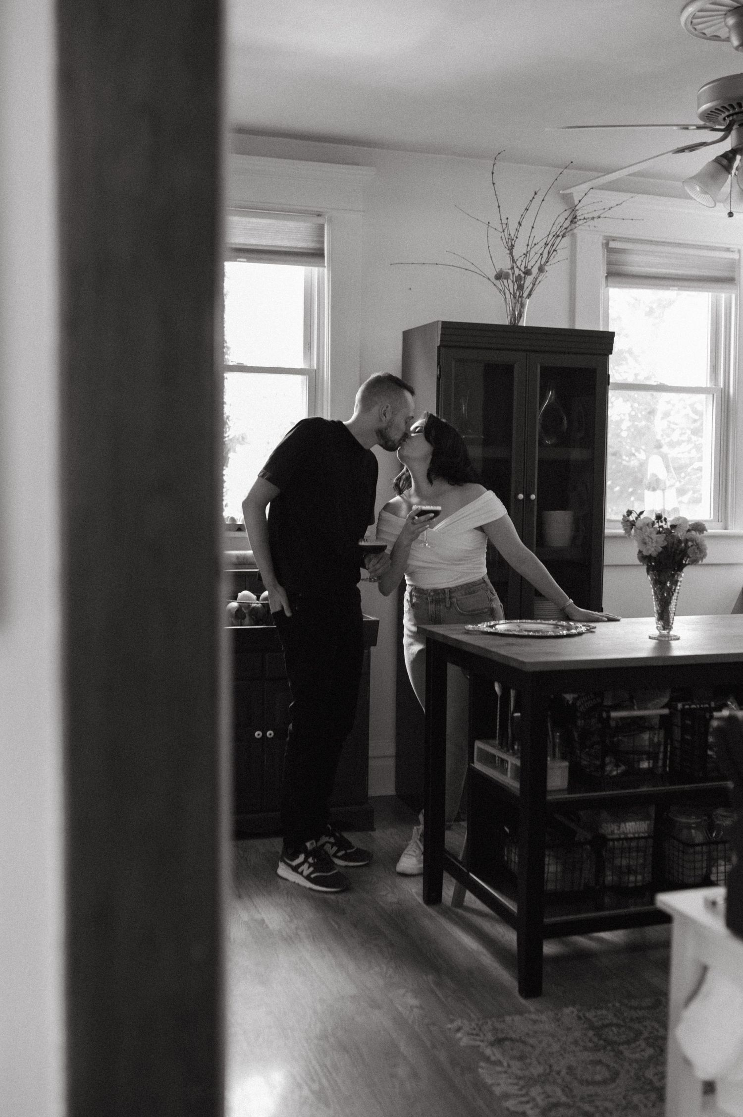 A black and white candid photo of two people in an intimate kitchen moment.