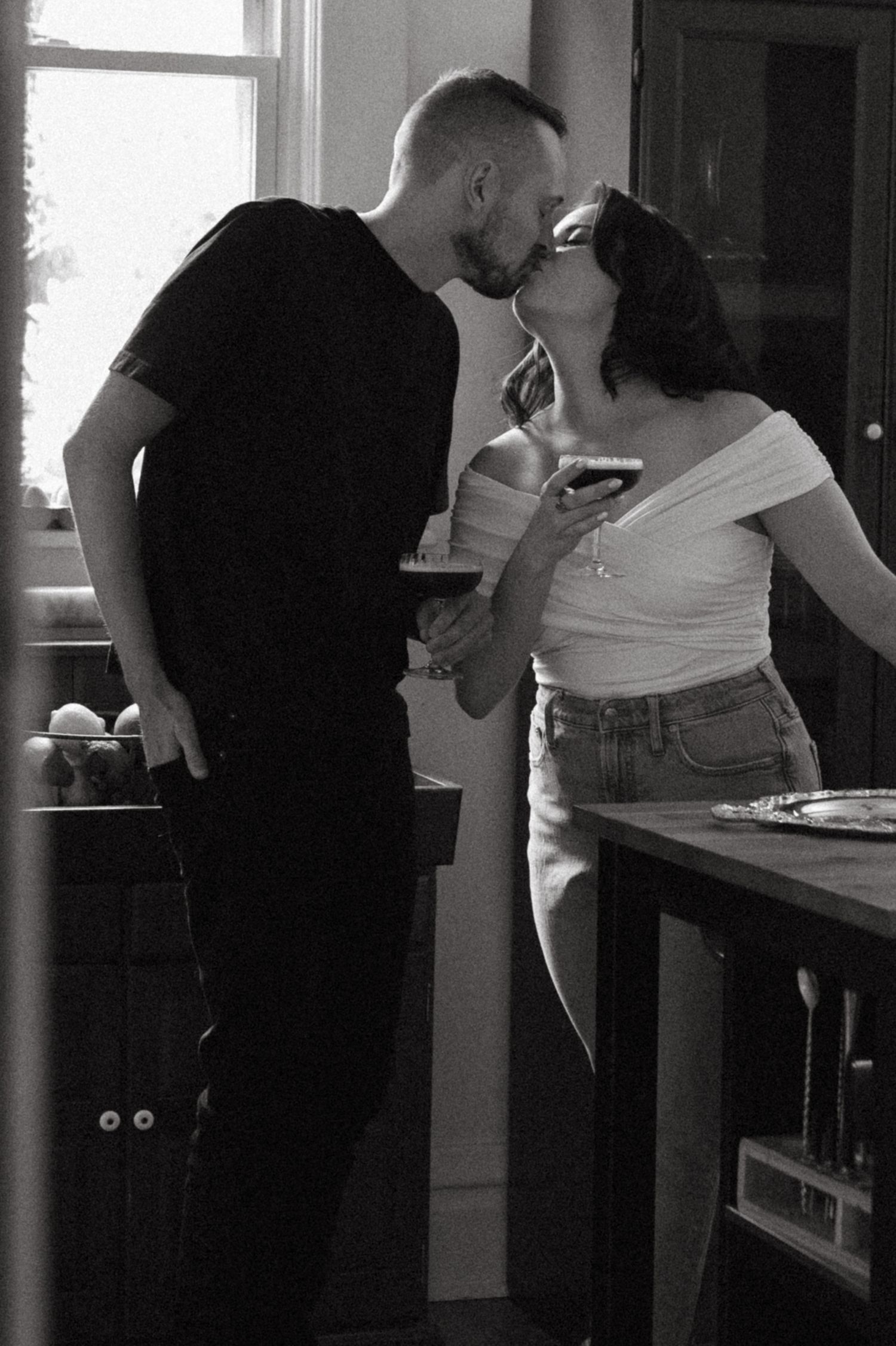 A romantic black and white photo of a couple sharing drinks in their kitchen.