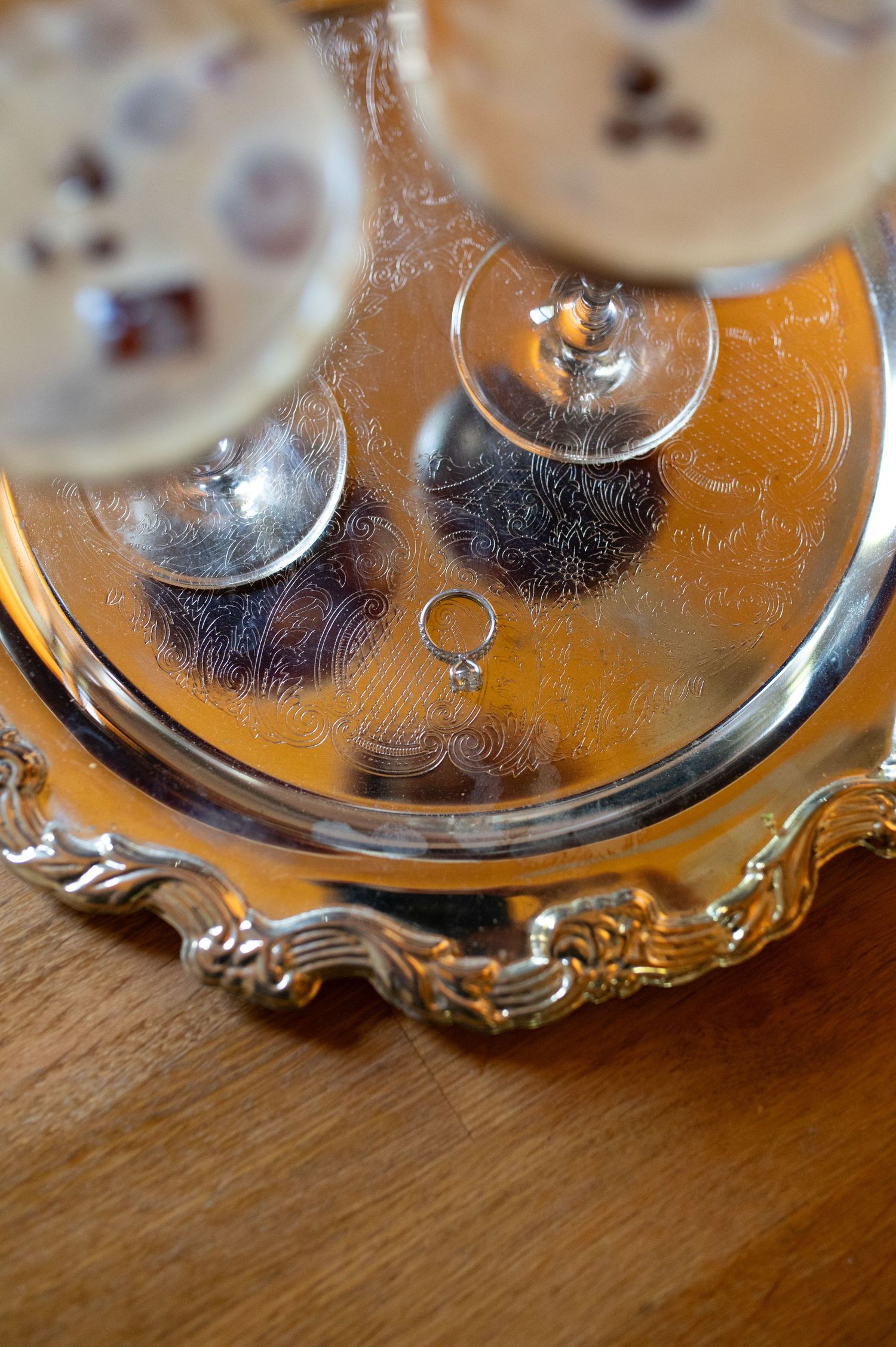 A silver decorative tray with champagne glasses and a small ring displayed on its ornate surface.
