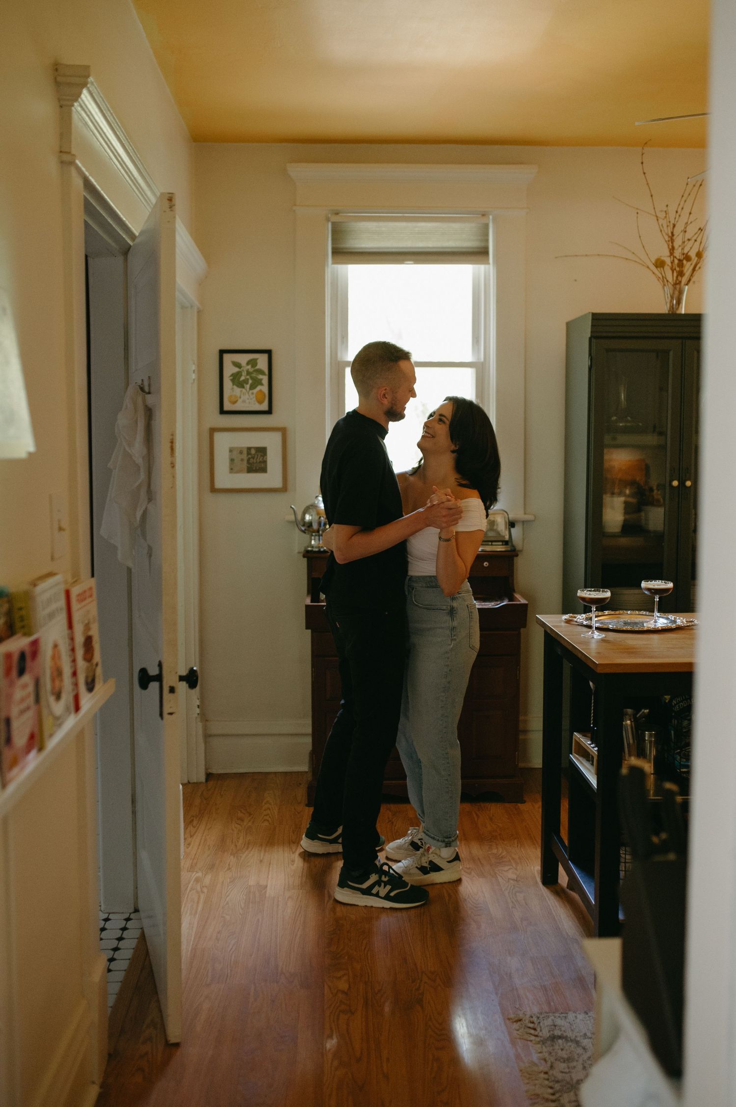 A couple sharing an intimate moment in their apartment hallway with warm lighting.