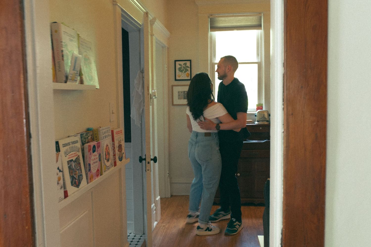 A tender embrace captured in a cozy home hallway with white walls and hardwood floors.