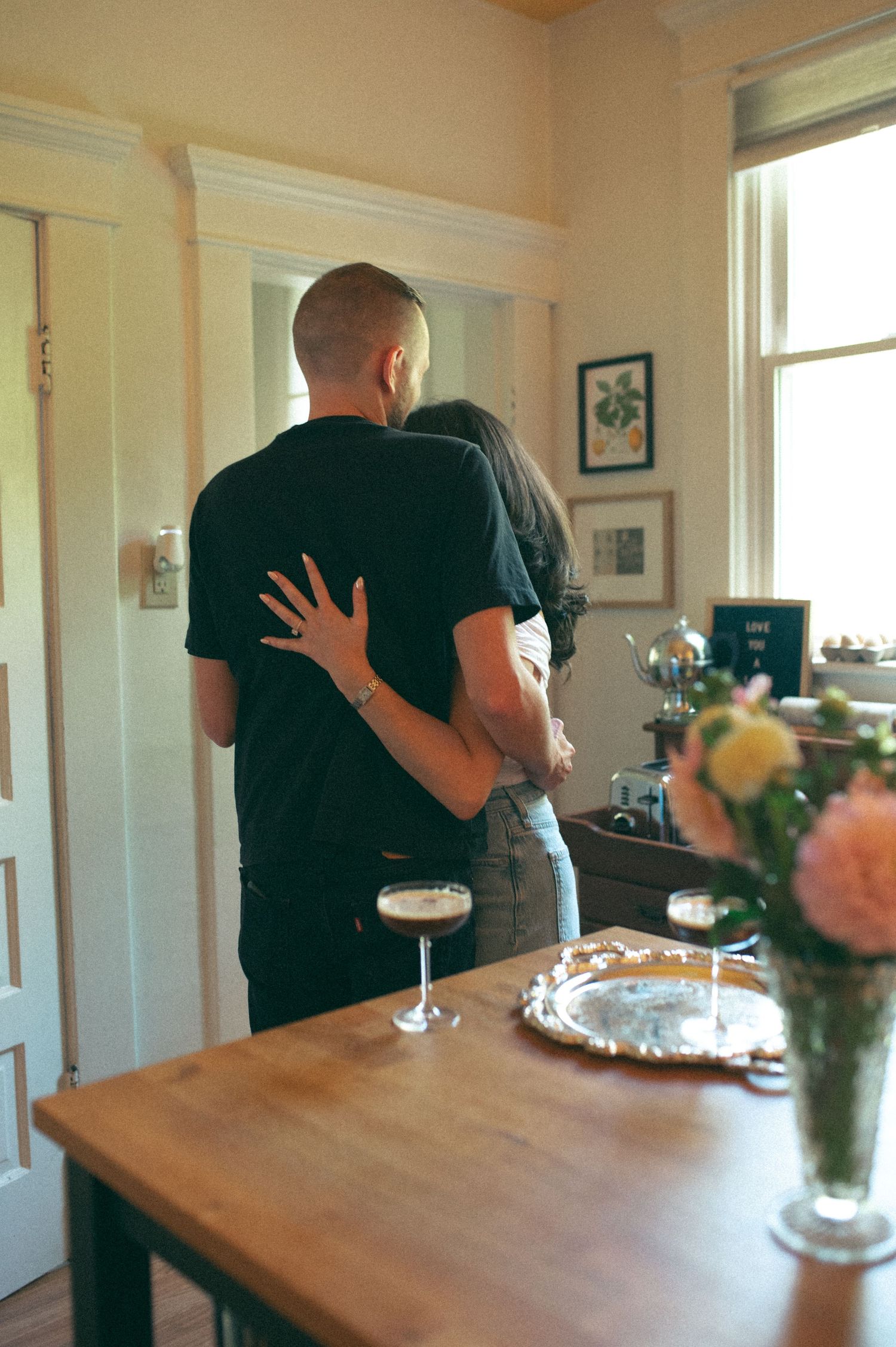 A couple sharing a romantic moment in their dining room with champagne glasses and flowers on the table.