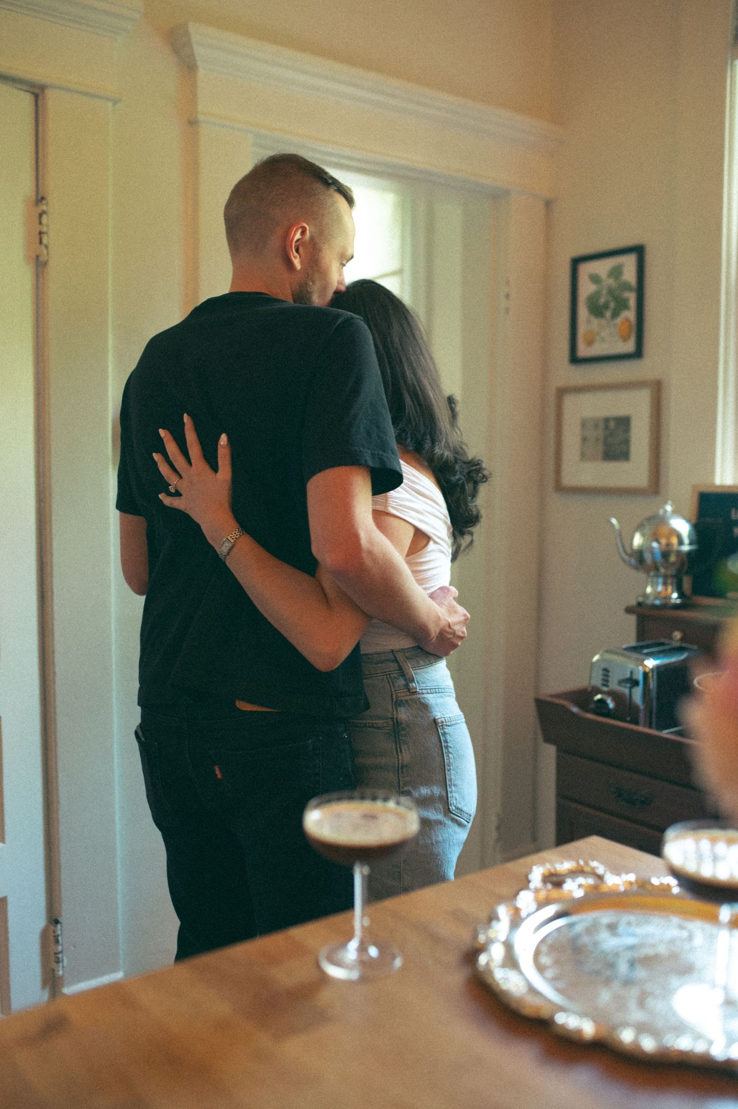 A sweet embrace near a dining table with champagne glasses and a decorative silver tray.