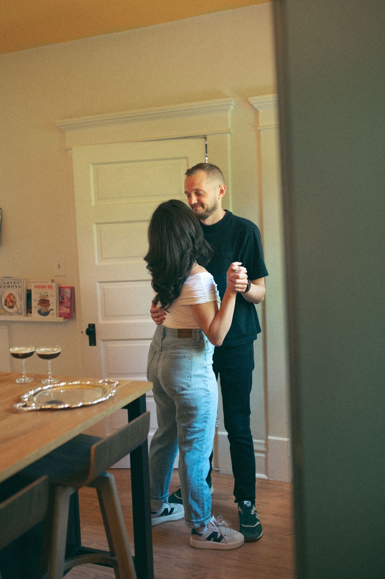 A couple dancing together in a sunlit dining room with hardwood floors.