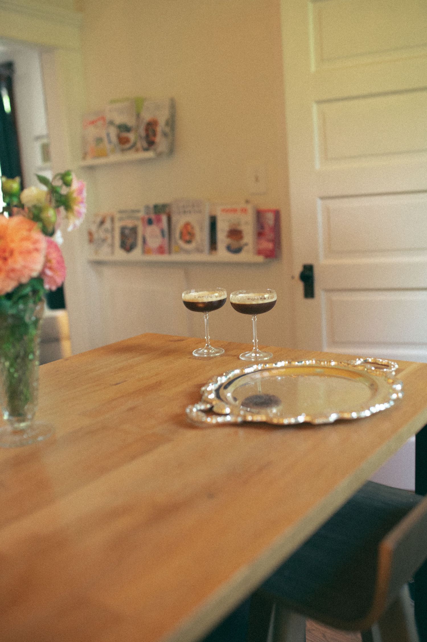 Two champagne glasses and a silver tray on a wooden dining table with fresh flowers in a vase.