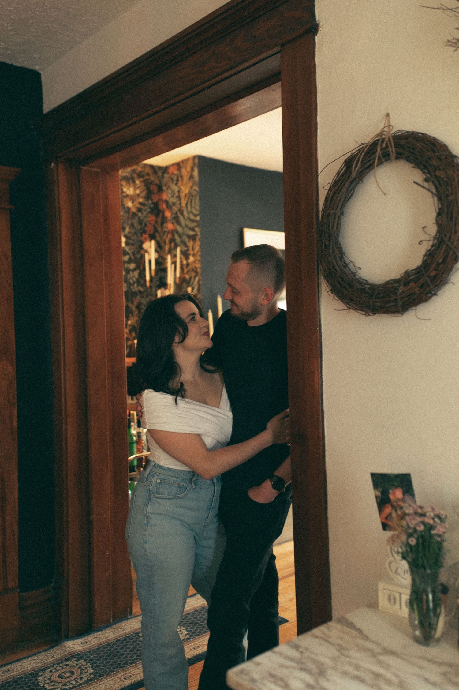 Romantic moment captured in a doorway with floral wallpaper and rustic decor visible.