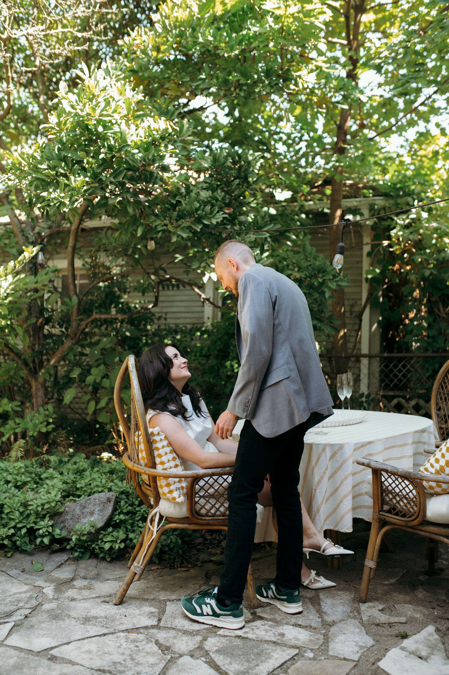 Romantic garden scene with couple at a white-clothed table surrounded by green foliage.
