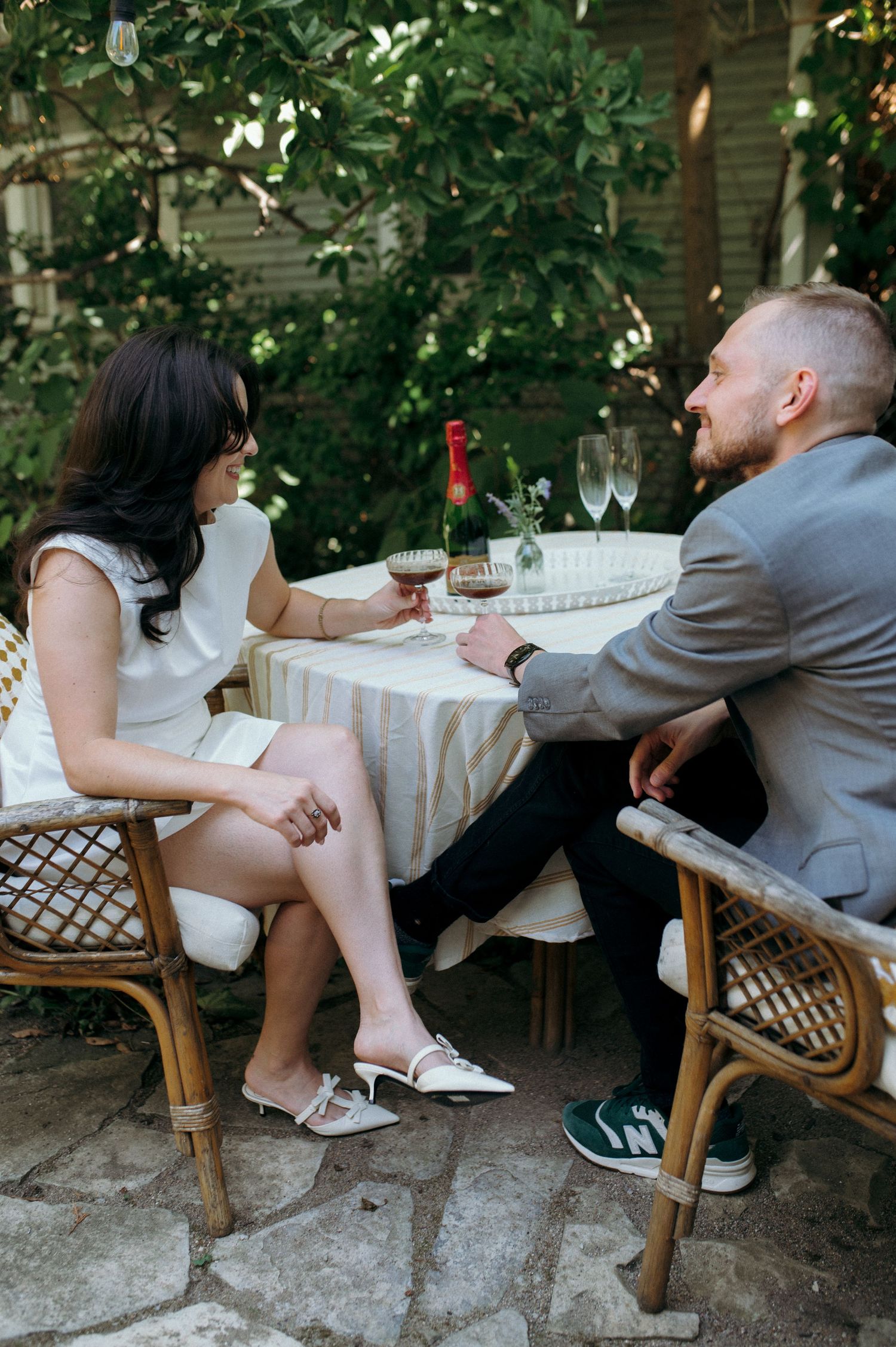 Couple enjoying wine at intimate outdoor table setting with rattan chairs and stone patio.