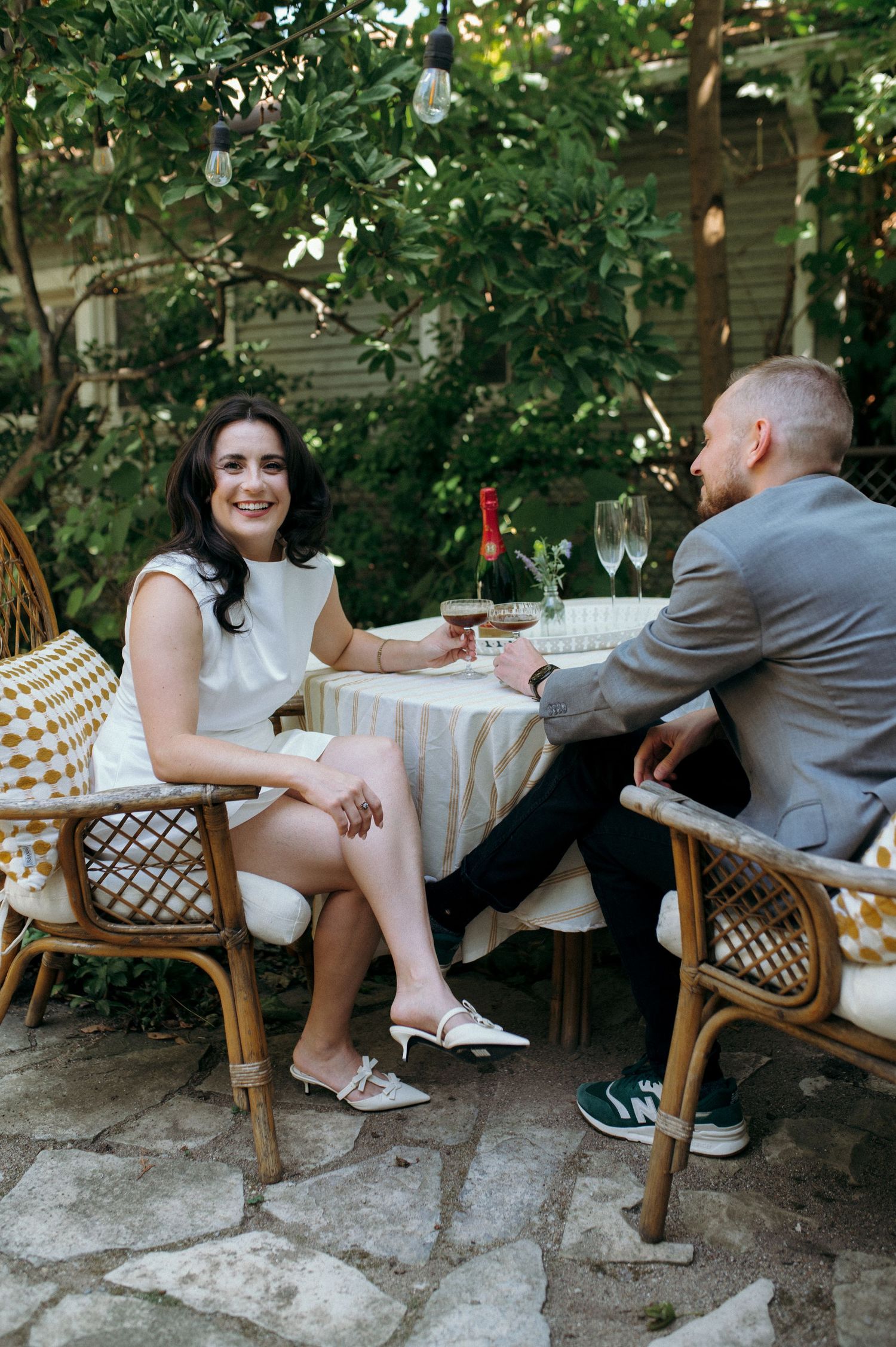 Garden dining scene with couple seated at white-clothed table surrounded by greenery.