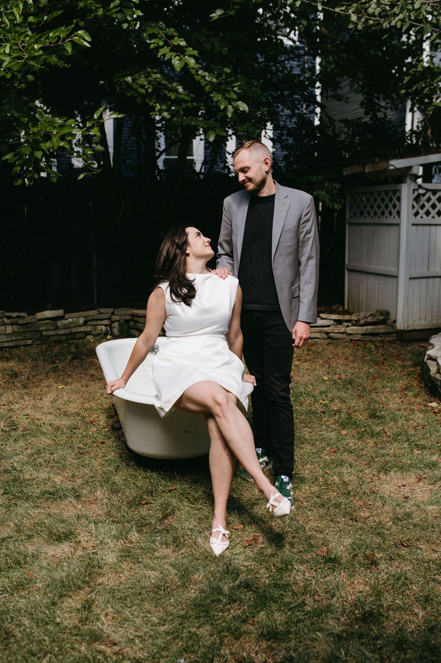A couple posing playfully with a vintage bathtub in a backyard garden setting.