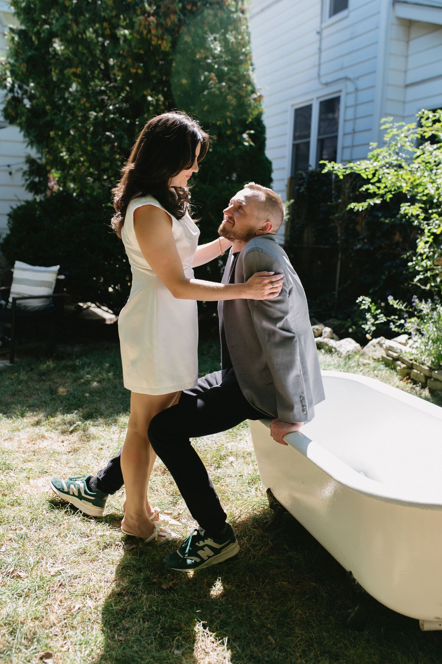 A playful moment captured between a couple dancing near a vintage bathtub outdoors.