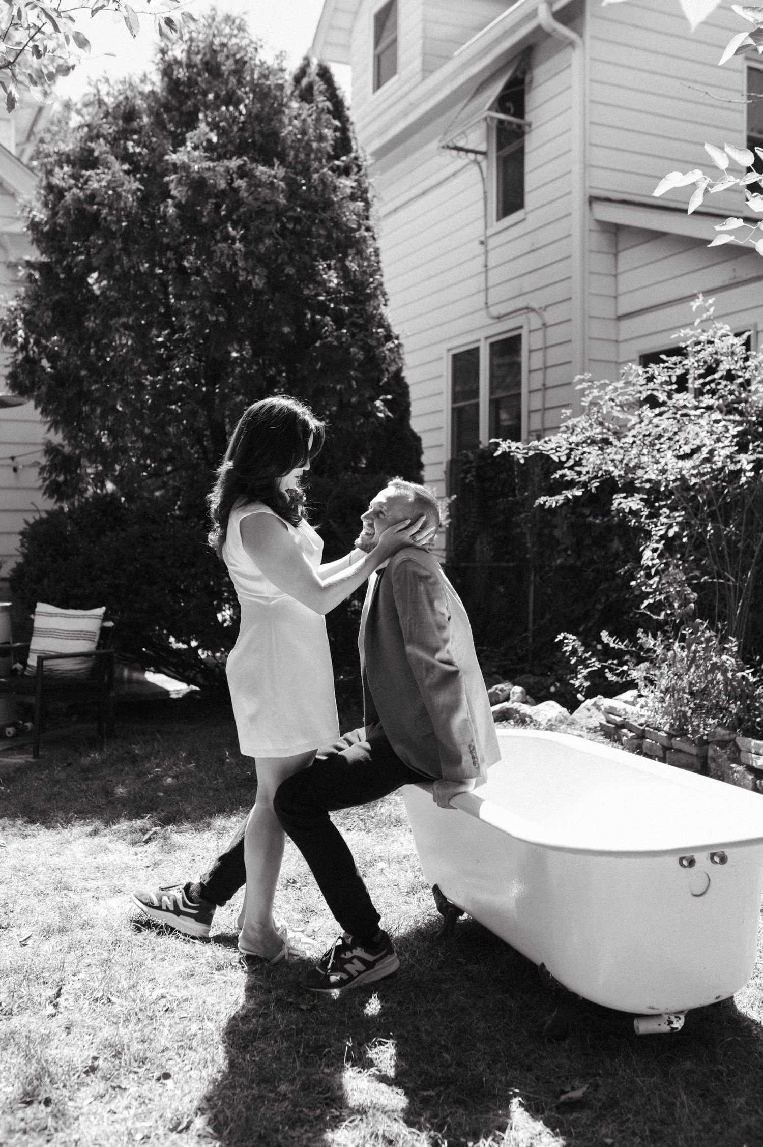 Black and white photo of a couple dancing beside a vintage bathtub in a garden setting.