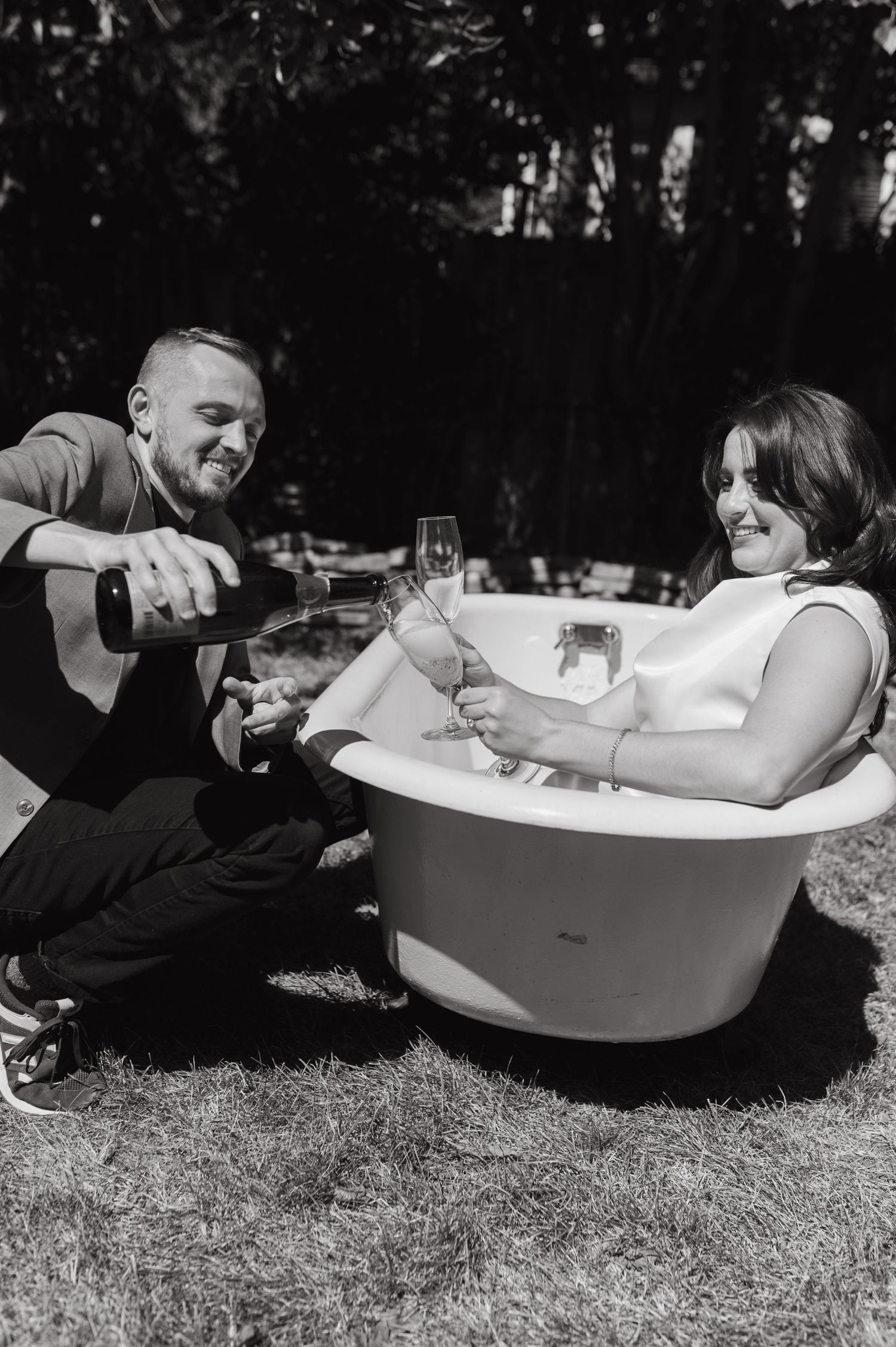 Couple enjoying champagne together in a unique outdoor bathtub setup on a sunny day.