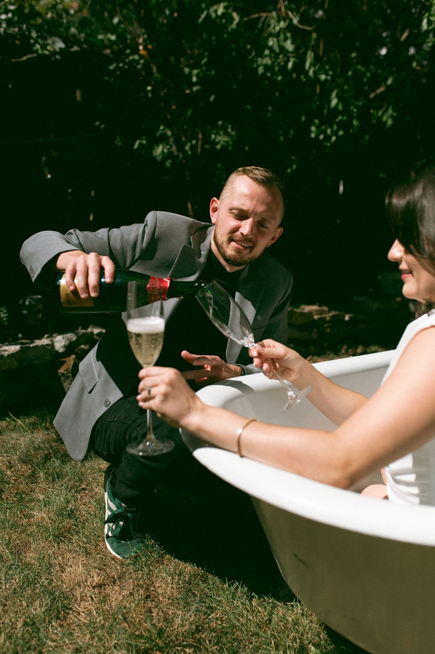 Pouring champagne outdoors while relaxing in a freestanding white bathtub.