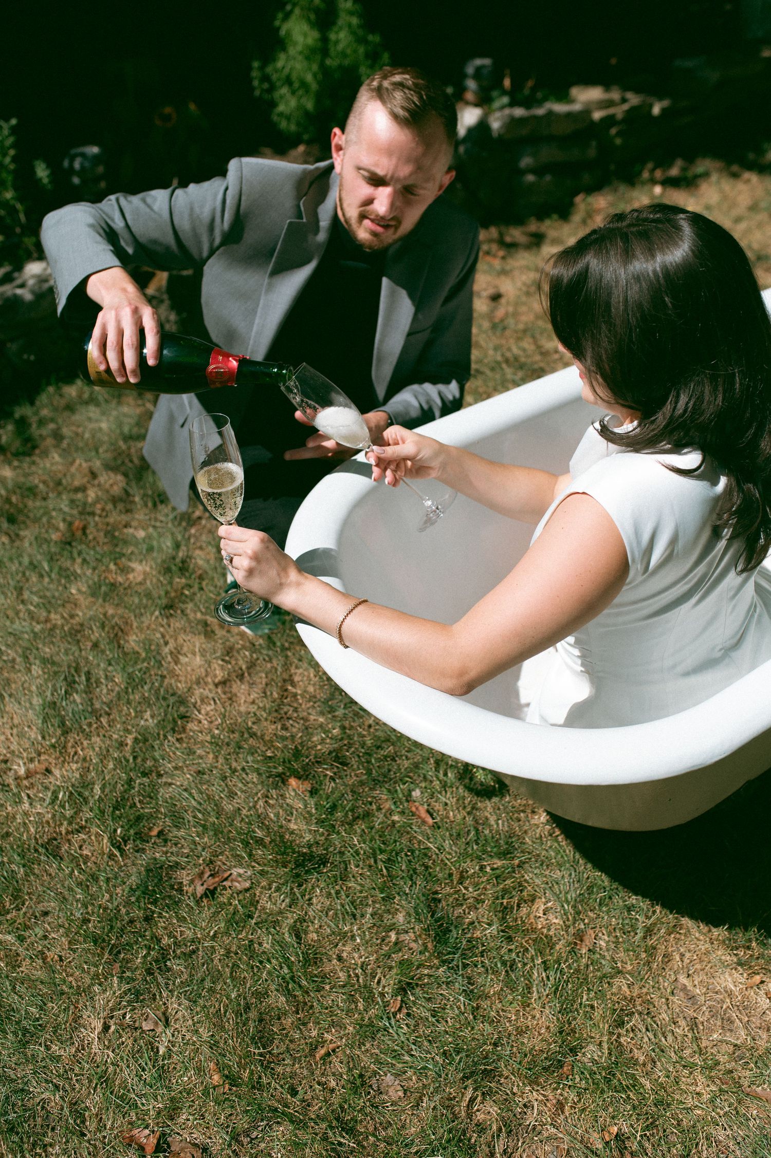 Creative outdoor photoshoot featuring champagne service by a bathtub in a garden setting.