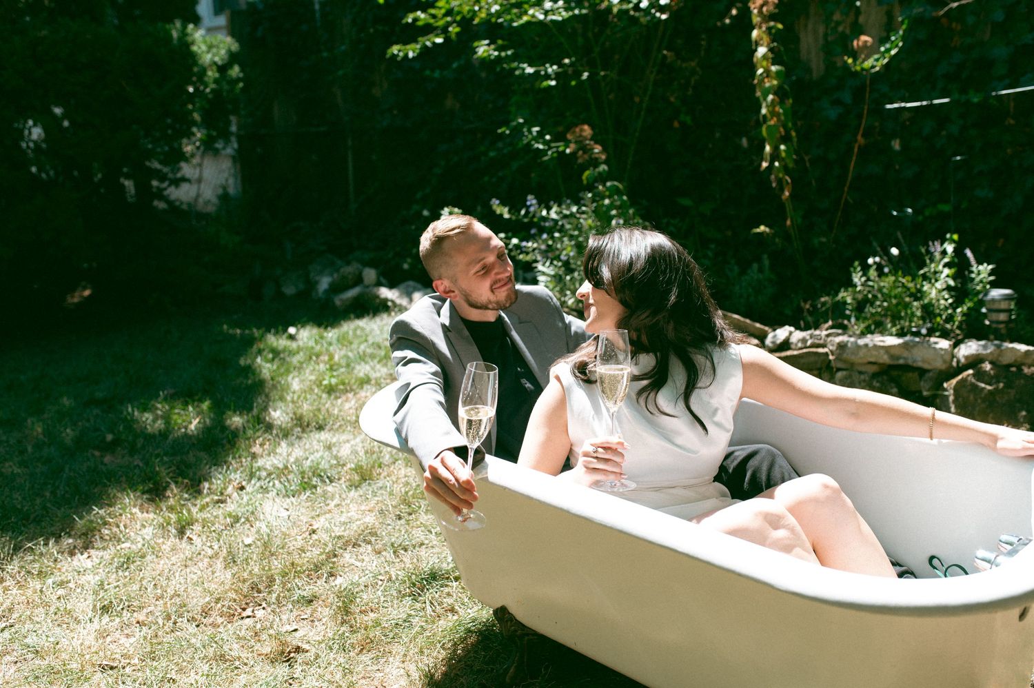 Romantic outdoor moment shared in a white bathtub under sunlit trees.