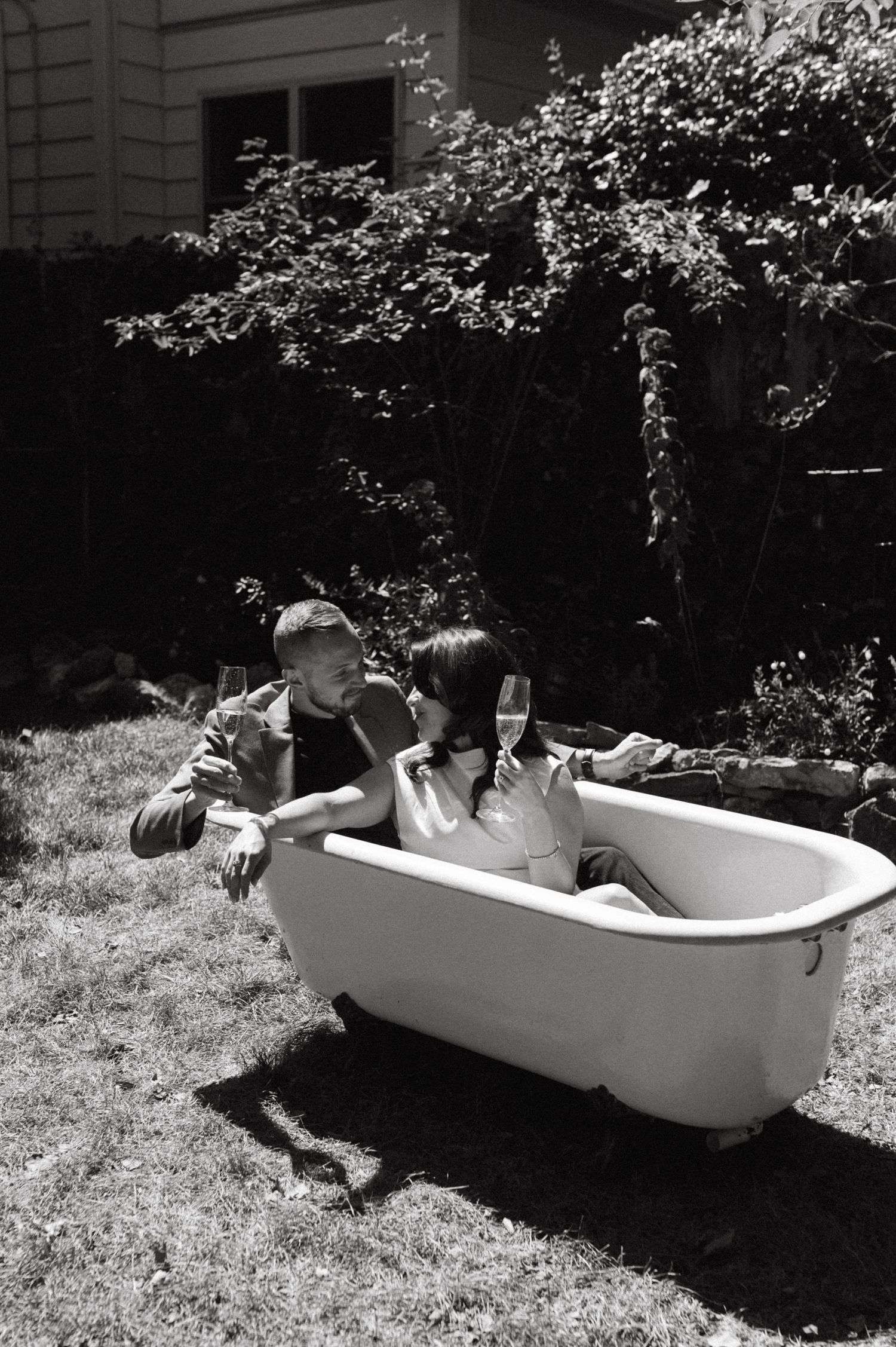 Playful outdoor bathtub scene with champagne in a backyard garden setting.