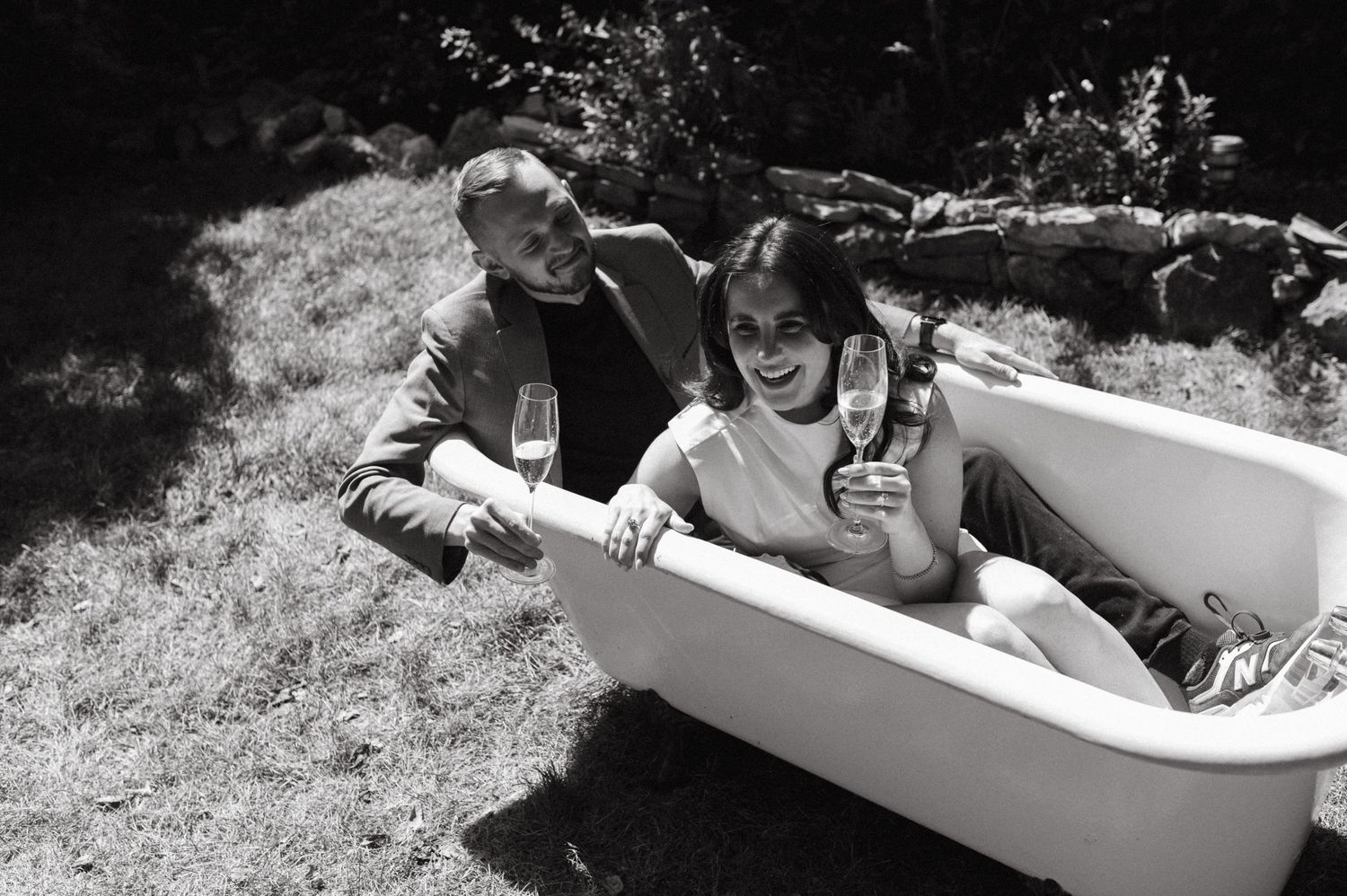 Candid moment of couple laughing and drinking in outdoor bathtub.
