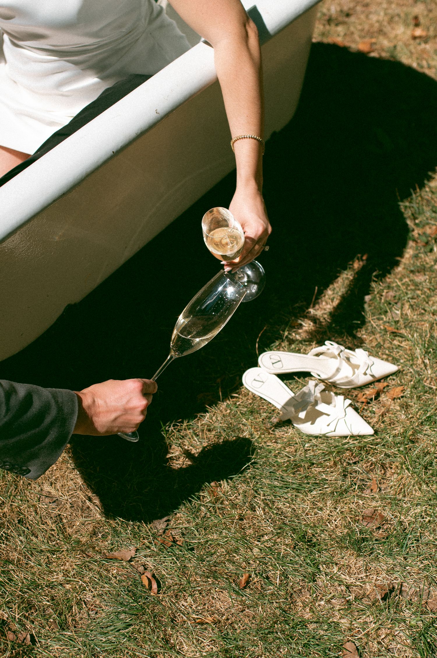 Close-up of champagne being poured next to white bathtub outdoors.