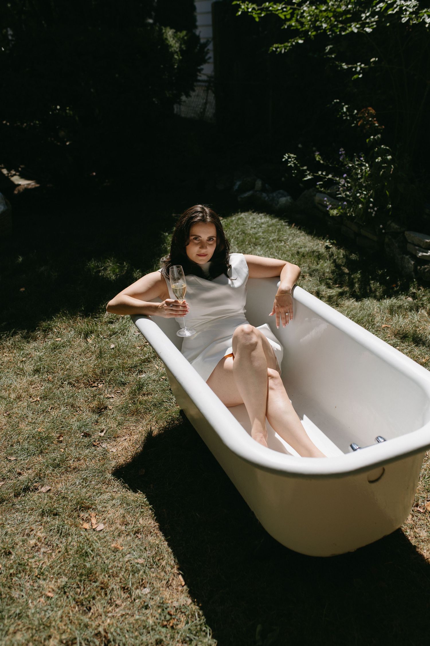 Woman in white dress relaxing in outdoor bathtub with champagne.