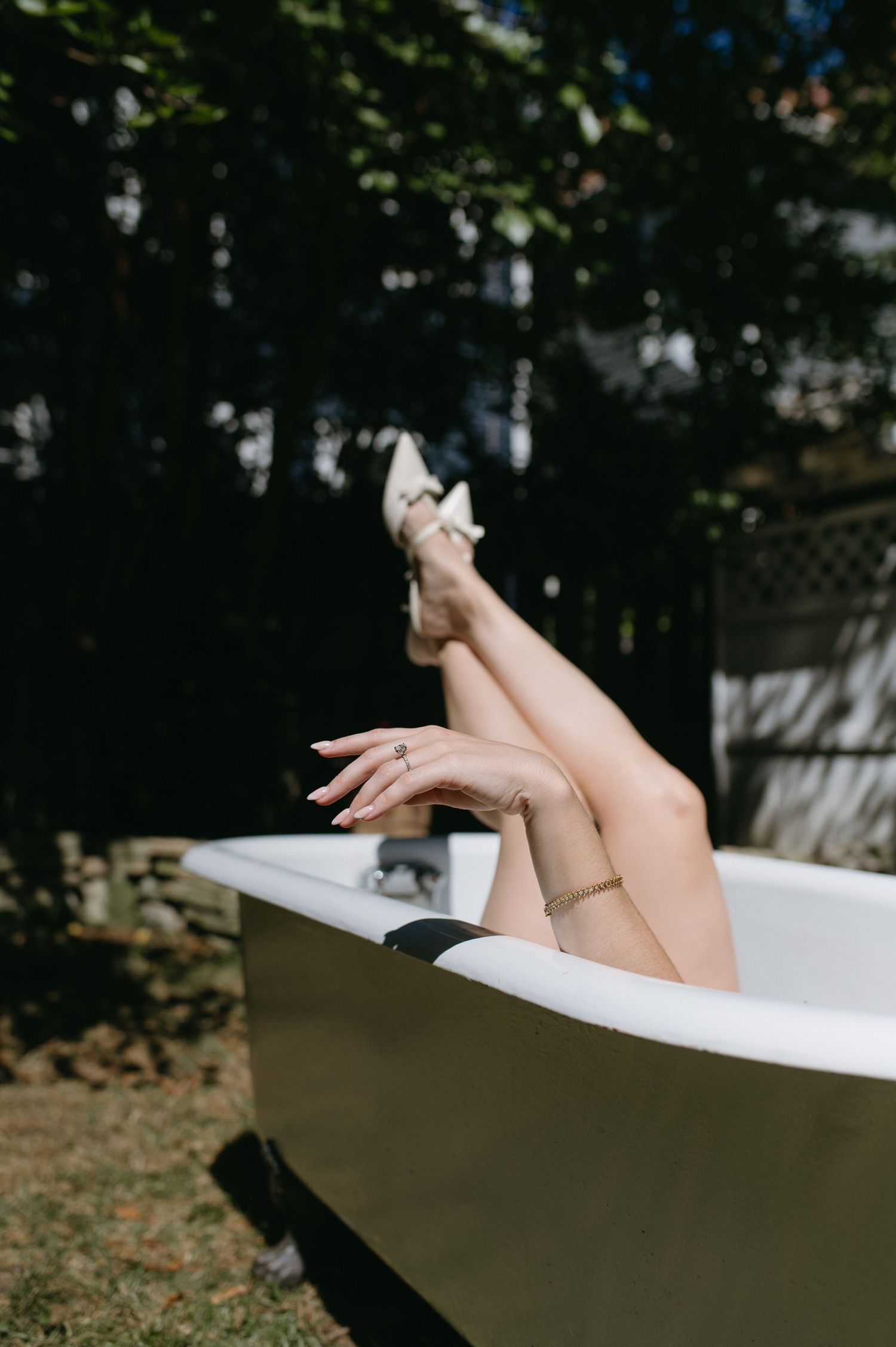 Legs with white shoes raised elegantly from a classic bathtub in a garden setting.
