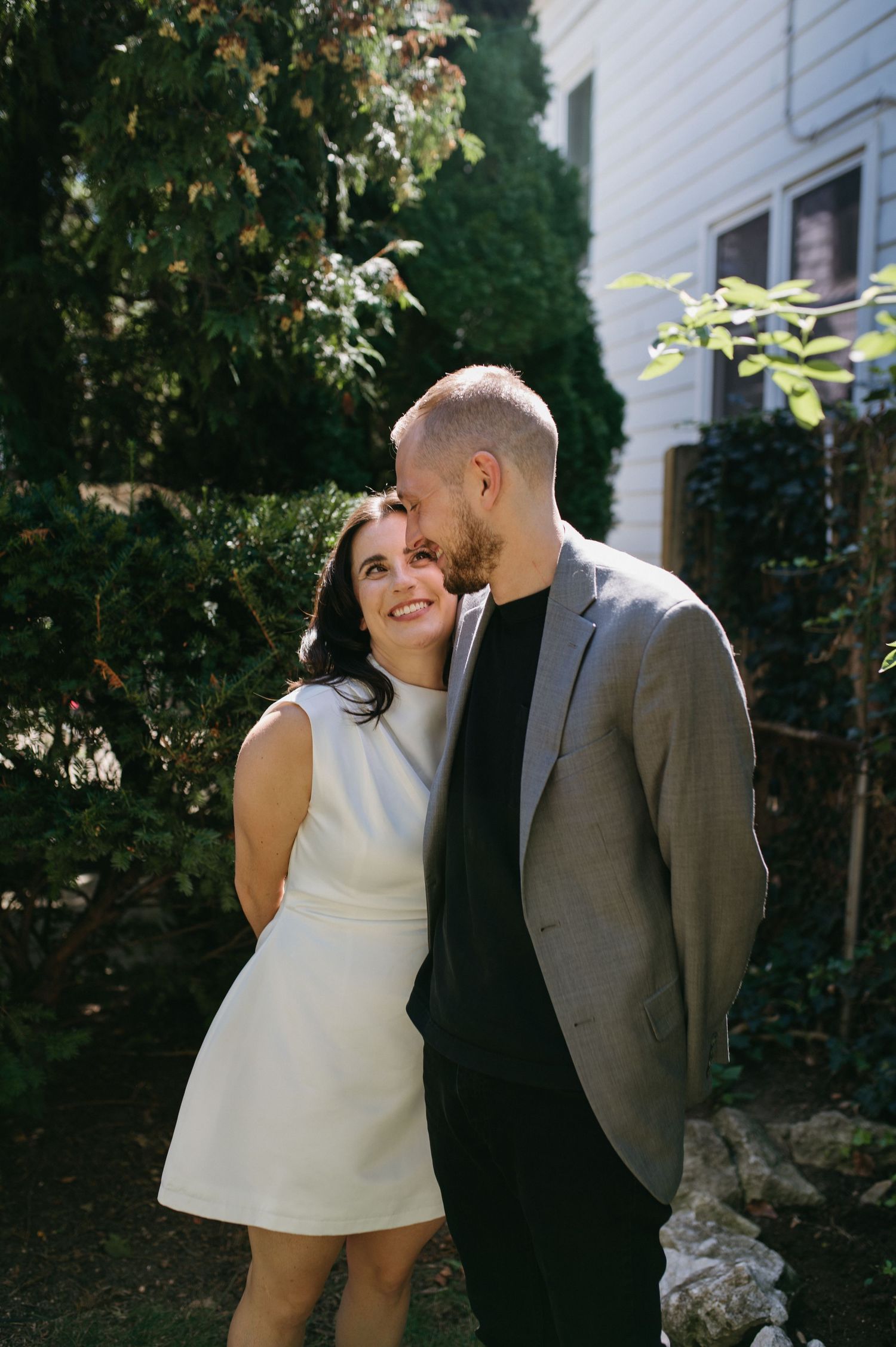 A romantic moment captured between a couple on a sunny day in front of a white house.