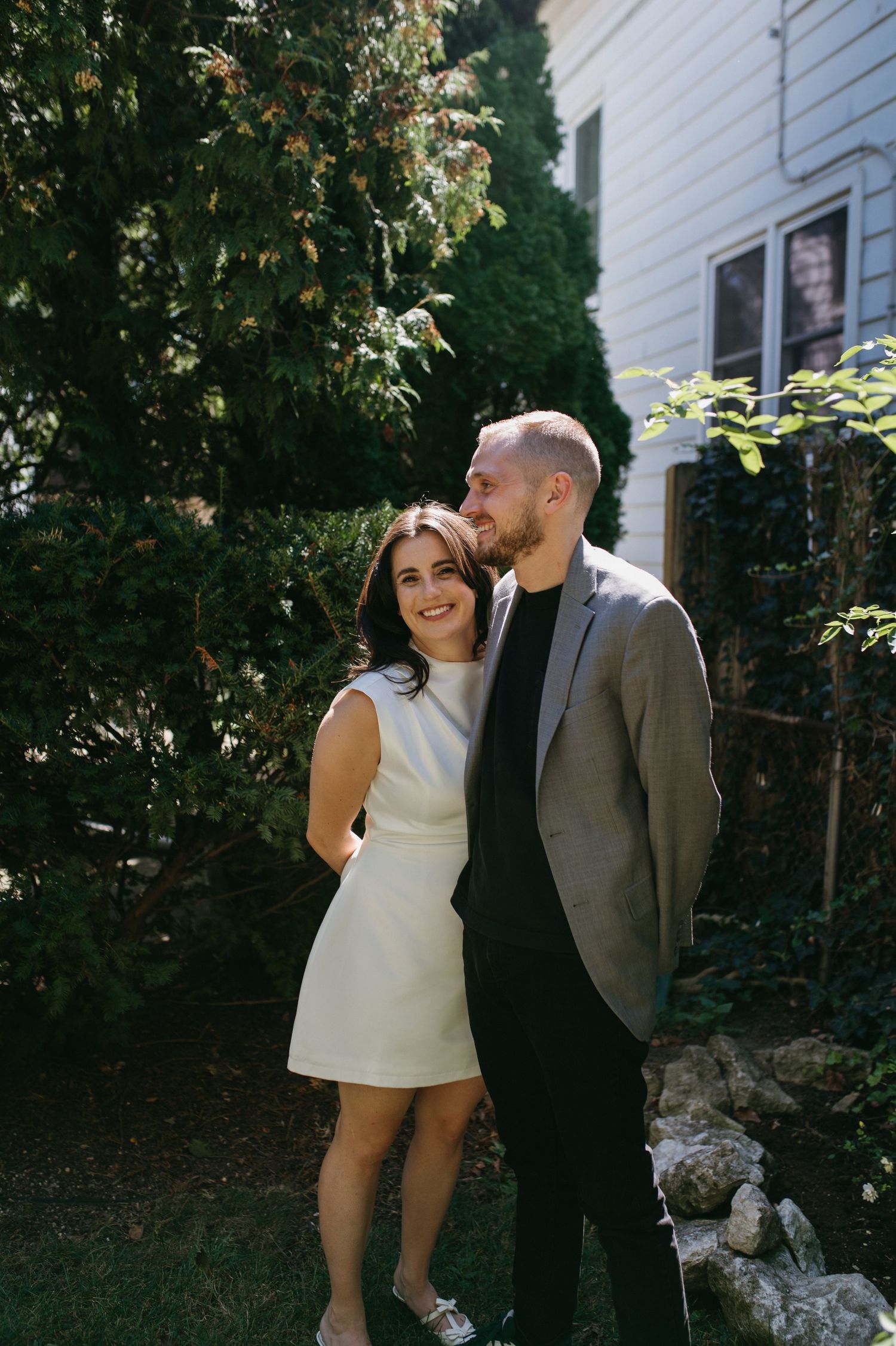 A tender moment shared between a couple in formal attire against a white house backdrop.