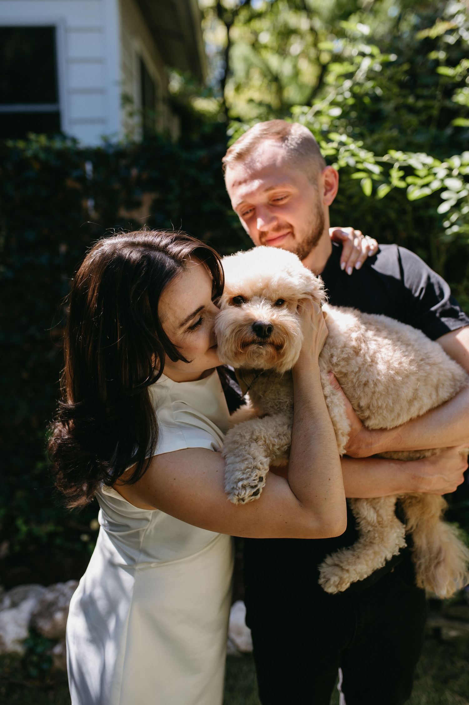 A couple shares a joyful moment with their fluffy goldendoodle dog outside their home.