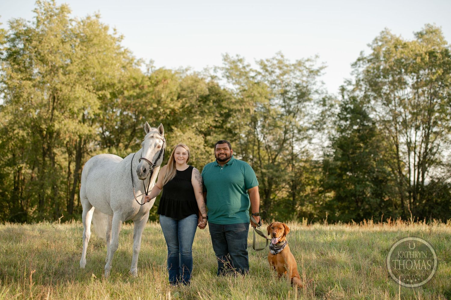 A white horse and redbone hound join their owners for a portrait in a sunlit meadow.