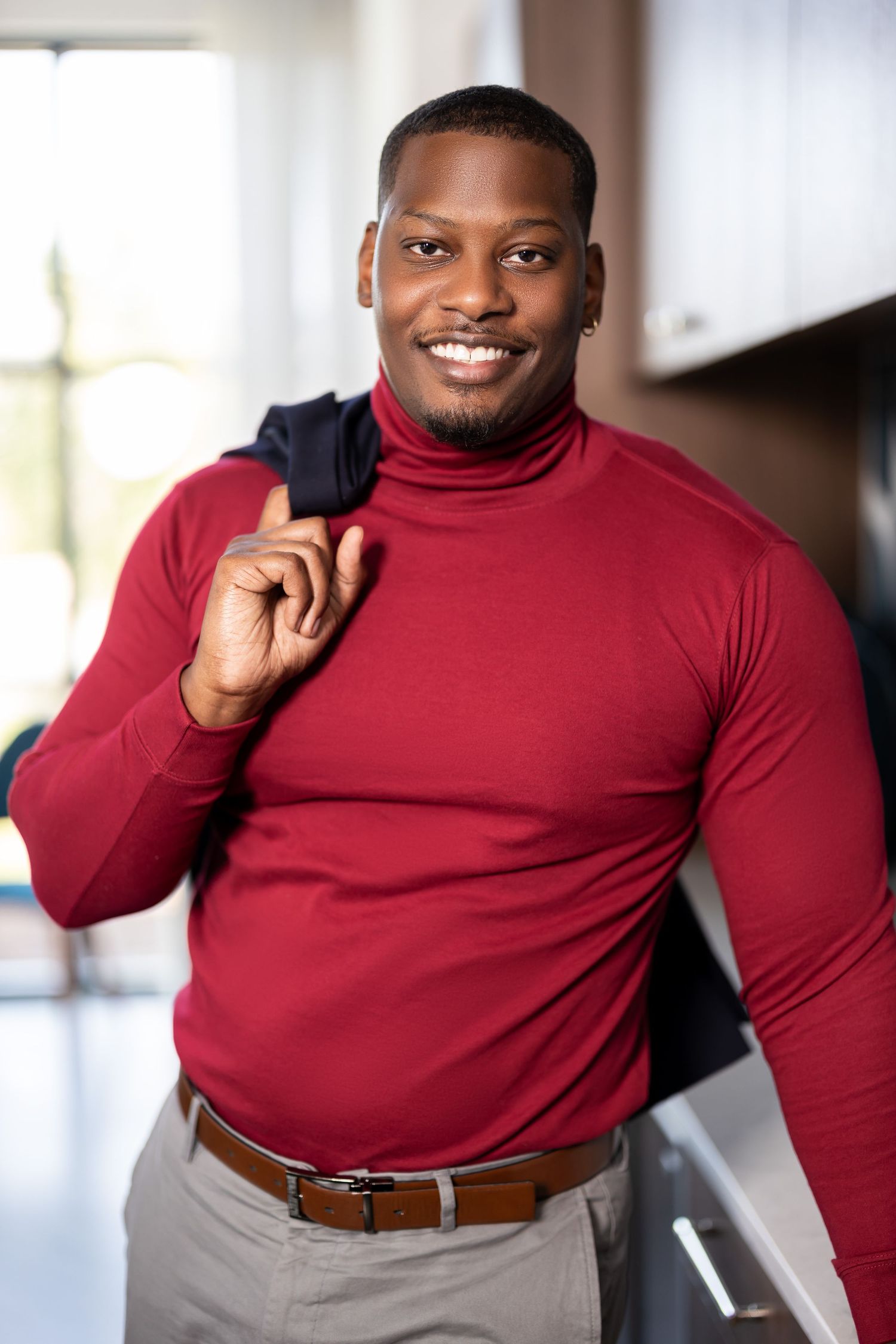 Professional in red turtleneck and khaki pants with jacket over shoulder.