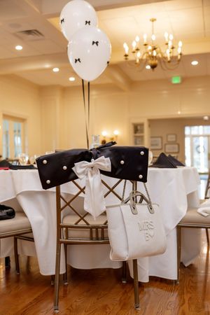 Bridal shower chair decorated with black bow, white balloons, and Mrs. tote bag.