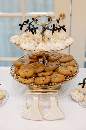 Gold tiered dessert stand with chocolate chip cookies, cake pops, and wedding dress shaped cookies.